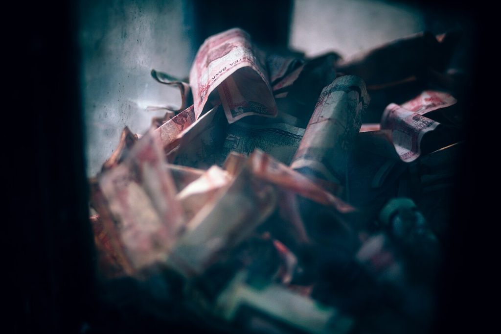 A pile of crumpled pink and red banknotes lying scattered in dim light.